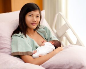 Mother smiling while breastfeeding a newborn baby, still at the hospital soon after birth.