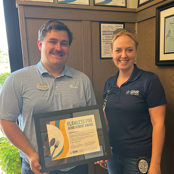 Restaurant staff and GNR Public Health inspector pose with a framed and signed Flawless Five Achievement Award certificate.