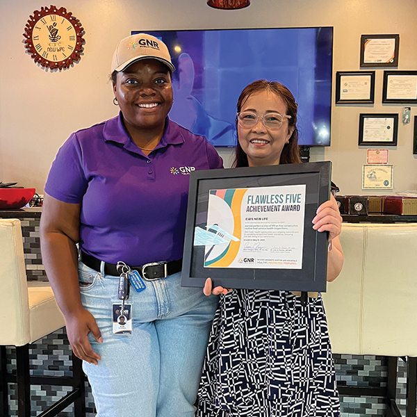 Restaurant staff and GNR Public Health inspector pose with a framed and signed Flawless Five Achievement Award certificate.