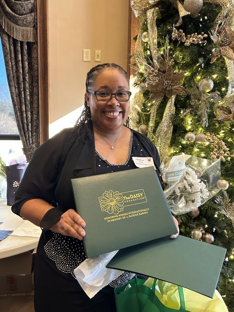 ShaRina Neal, RN, standing in front of a decorated pine tree, holding her DAISY Award.