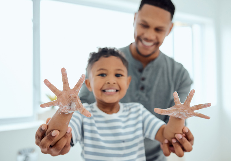 Child shows his soap covered hands while dad smiles in the background