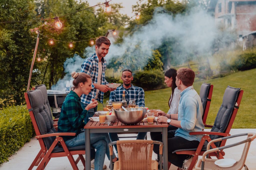 Group of young diverse friends seated at a table on a patio, enjoying a cookout together