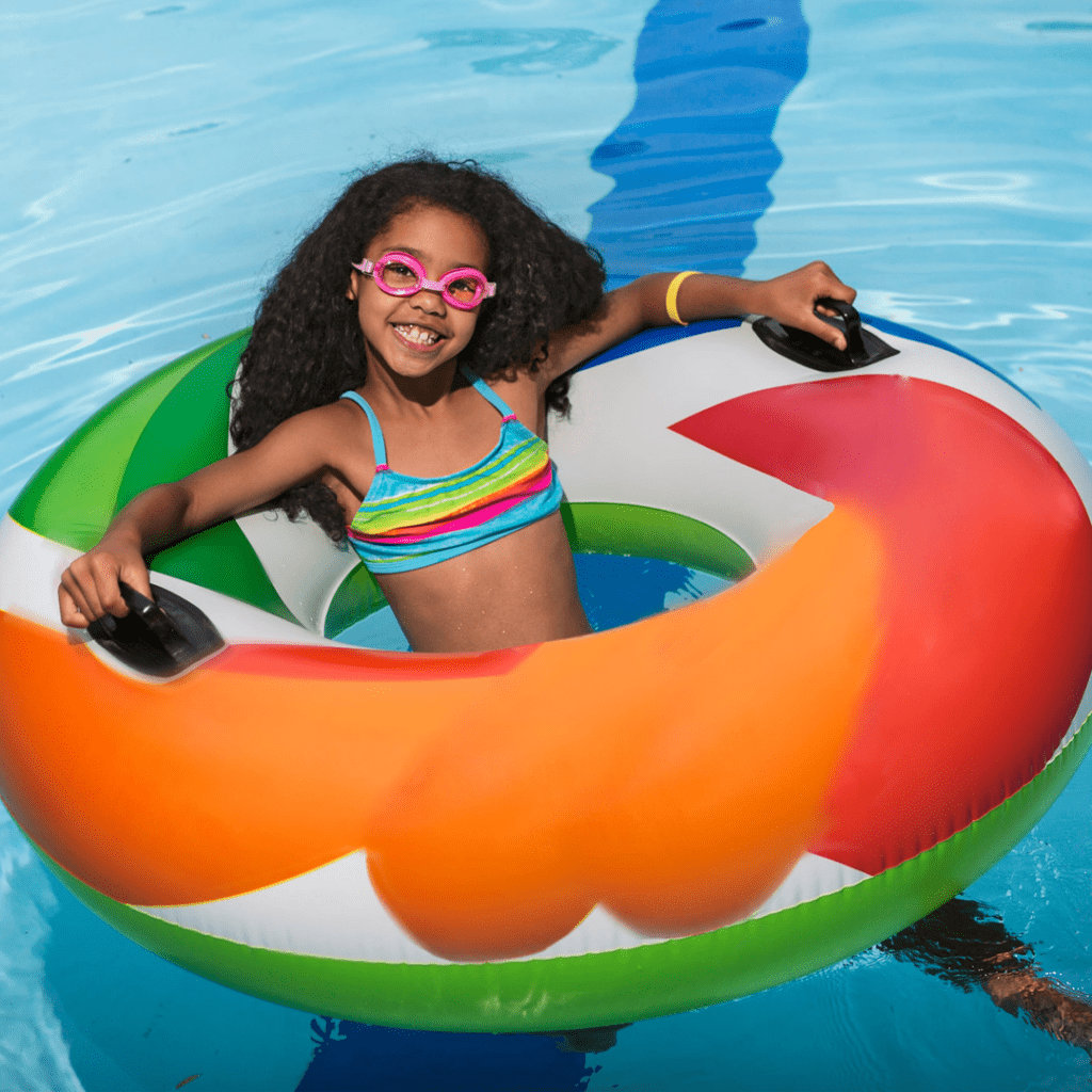Smiling school-age girl floating in a swimming pool inside a floatie.