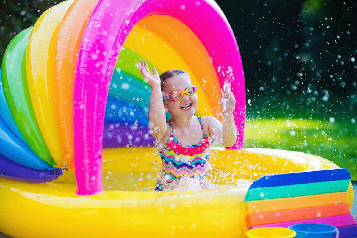 Little girl wearing a swimsuit and googles splashes inside a blow-up pool.